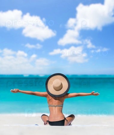 Happy freedom carefree bikini woman enjoying summer beach vacation with arms up cheering in success. Girl feeling free with sun hat relaxing sunbathing on holidays. Caribbean south tropical travel.