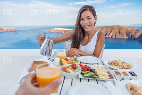 Couple eating breakfast. Smiling tourist woman drinking coffee and man drinking orange juice on terrace resort outdoor. Healthy and delicious food served for breakfast. Santorini, Greece.