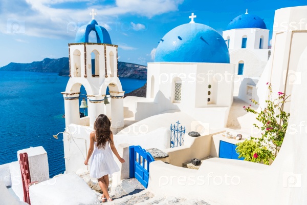 Santorini travel tourist woman on vacation in Oia walking on stairs. Person in white dress visiting the famous white village with the mediterranean sea and blue domes. Europe summer destination.