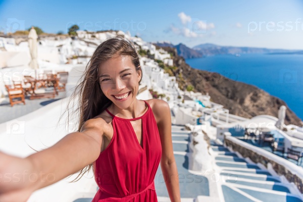 Travel Vacation Tourist Selfie. Woman taking self-portrait photo on Santorini, Greek Islands, Greece, Europe. Girl on summer vacation visiting famous tourist destination having fun smiling in Oia.