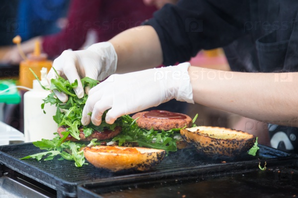 Chef making beef burgers outdoor on open kitchen international food festival event. Street food ready to serve on a food stall, stock photo