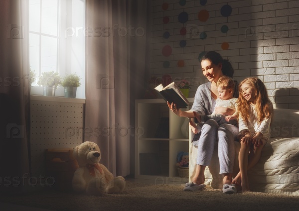 Family reading bedtime. Pretty young mother reading a book to her daughters, stock photo