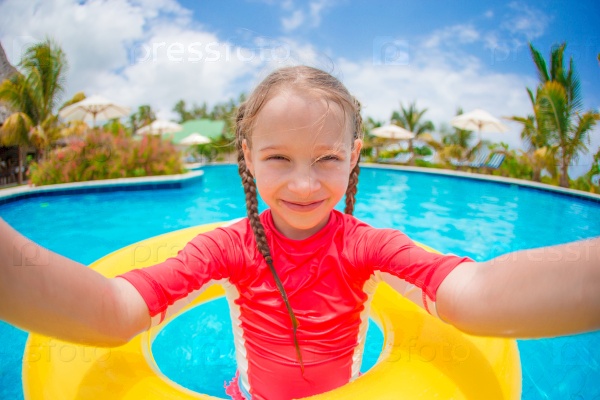 Little girl making selfie at inflatable rubber ring in swimming pool, stock photo