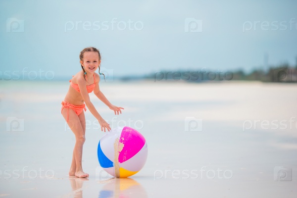 Little girl playing with air ball on white beach, stock photo