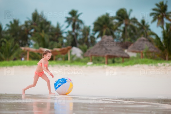 Little girl playing with big air ball on white beach, stock photo