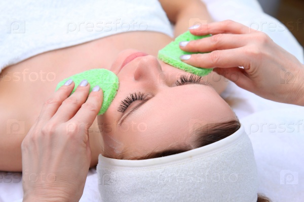 Beautician makes cleansing and exfoliating facial for beautiful girl. Beauty salon, stock photo