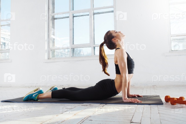 Beautiful young slim woman doing stretching exercises at the gym with orange dumbbells, stock photo