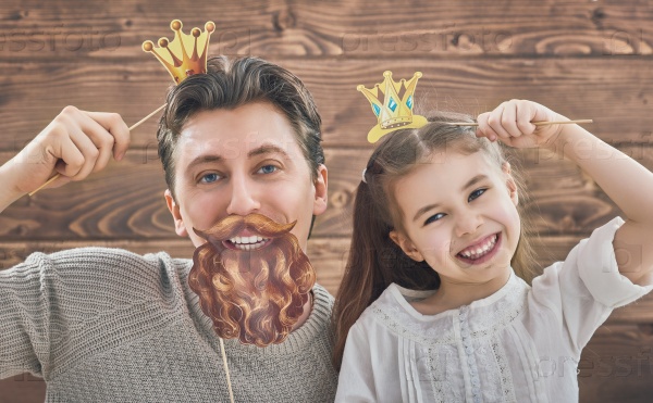 Funny family! Father and his child daughter girl with a paper accessories. Beauty funny girl holding paper crown on stick. Beautiful young man holding paper beard and crown on stick, stock photo