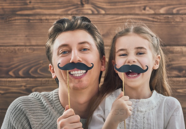 Funny family! Father and his child daughter girl with a paper accessories. Beauty funny girl holding paper mustache on stick. Beautiful young man holding paper mustache on stick.