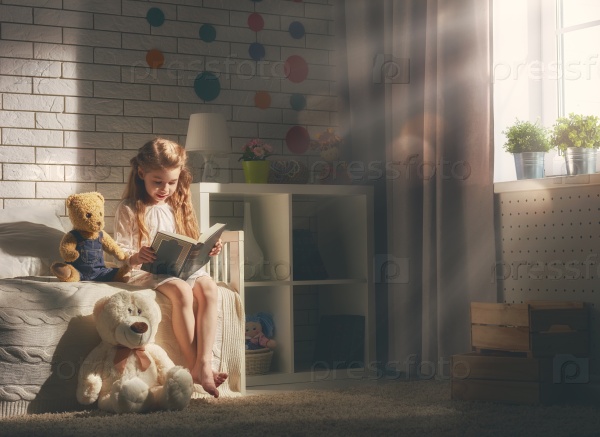 Cute little child girl reading a book. Kid girl sitting in her bed, stock photo
