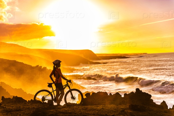 MTB cyclist mountain biking woman cycling looking at view on bike trail on coast at sunset. Person on bike by sea in sportswear with bicycle enjoying healthy active lifestyle in beautiful nature.