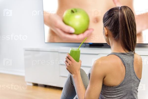 Healthy eating woman drinking green smoothie watching television online education tv show about nutrition and weight loss. Girl sitting at home learning about losing weight with vegetables and fruits.