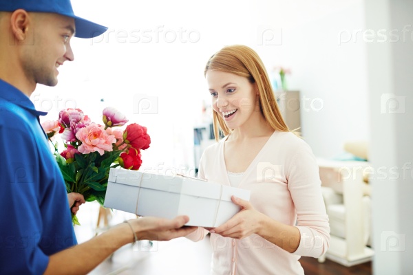 Delivery boy giving gift box and flowers to a surprised woman