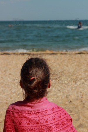 Young girl sits with his back to the camera in the sand on the beach on vacation and travel