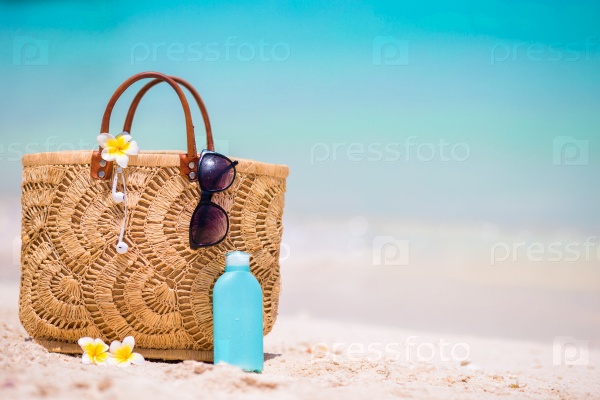 Beach accessories - straw bag, headphones, bottle of cream and sunglasses on the beach, stock photo