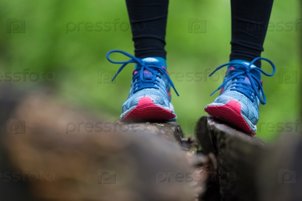 Adventure, sport and exercise. Detail of female legs wearing sport shoes standing on tree trunk in forest, stock photo