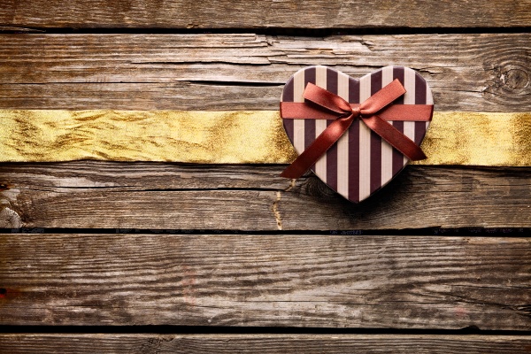 Heart shaped Valentines Day gift box with wrinkled golden ribbon on old wood. Vintage holiday background.