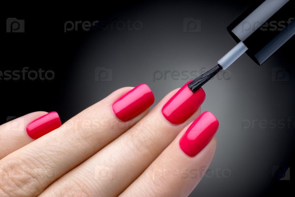 Beautiful manicure process. Nail polish being applied to hand, polish is a red color. Black background closeup.