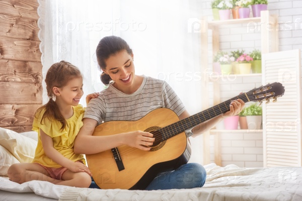 Happy family. Mother and daughter playing guitar together. Adult woman playing guitar for child girl.