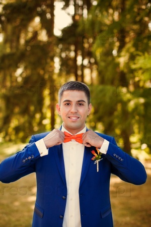 The groom holds a tie and smiles.Portrait of the groom in the park on their wedding day.Rich groom on their wedding day