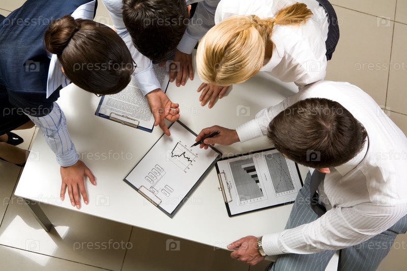 бизнесмен и двое сотрудников склонились над документами, решая рабочий вопрос