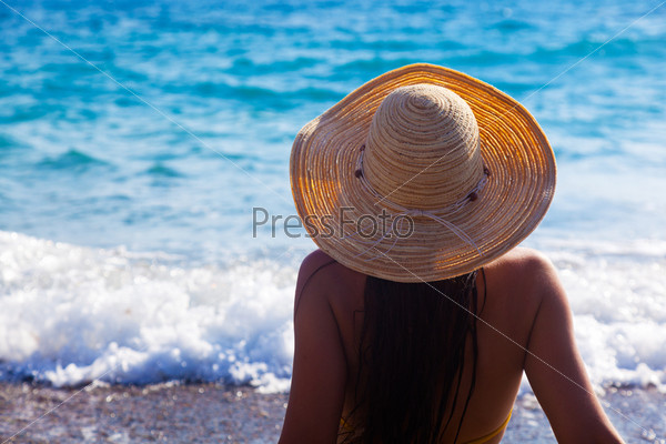 Стройная девушка в купальнике стоит на пляже. Вид сзади
