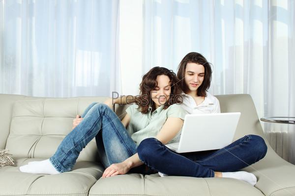 Фотография на тему Молодая пара сидит дома на диване и смотрит в ноутбук