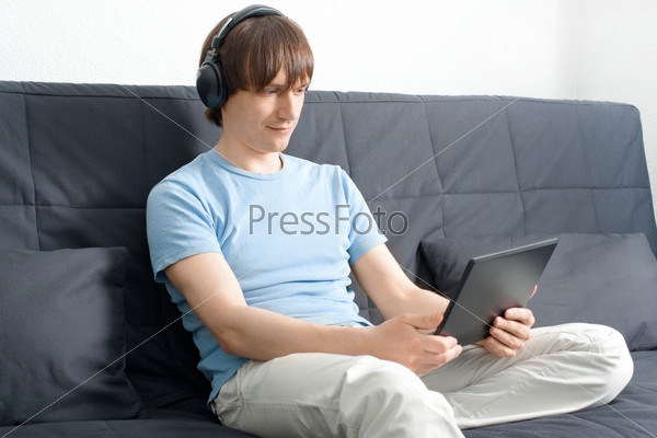 Фотография на тему Молодой человек сидит на диване с ноутбуком и слушаетмузыку в наушниках