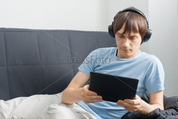 Фотография на тему Молодой человек сидит на диване с ноутбуком и слушаетмузыку в наушниках