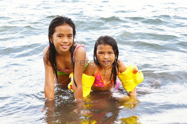Две девочки купаются на пляже и глядя на камеру.