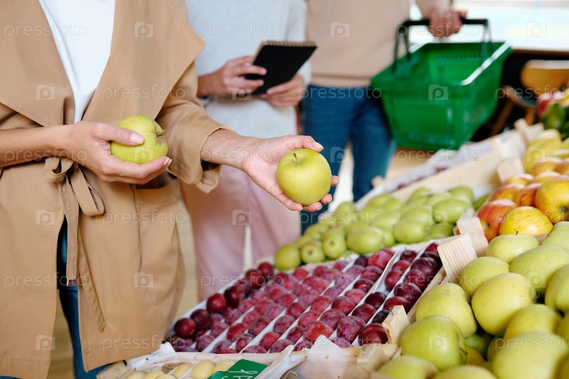 Young woman in beige trenchcoat holding two ripe granny smith apples