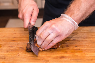 Повар в перчатках режет жареное мясо утки на деревянной разделочной доске - Spritnyuk