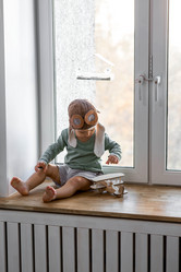 Милый 2-летний мальчик в кепке играет на подоконнике с деревянным самолетиком. Детские деревянные игрушки для развития ребенка - PhotoJuli