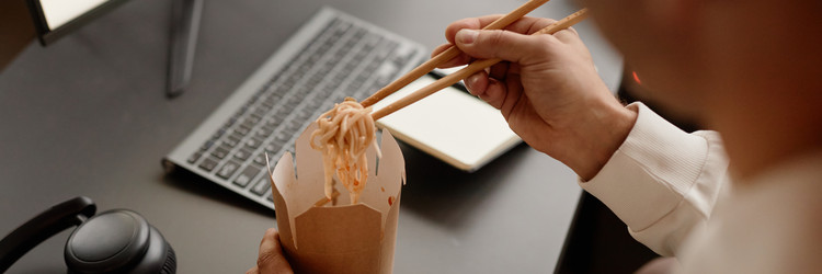 Header Image of Man Having Lunch at Work Eating Wok Noodles at Desk in Office Человек обедает на работе, ест ваковые лапши за столом в офисе - SeventyFour