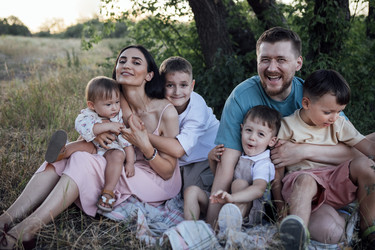 Семья наслаждается радостным моментом на природе, сидя на одеяле на травяном поле, в окружении природы, запечатлевая суть единения и счастья - Darya Petrenko