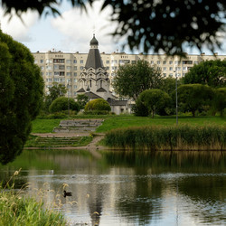 St George’s Church in Park Internatsionalistov, Saint Petersburg, framed by trees and pond water with Soviet apartment blocks in background - ezolyzm
