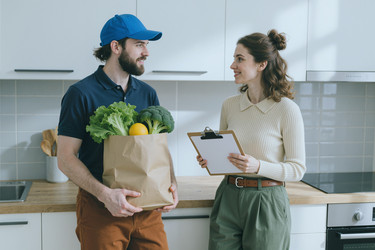 Взрослый курьер передает женщине продуктовый заказ дома. - AnnaStills