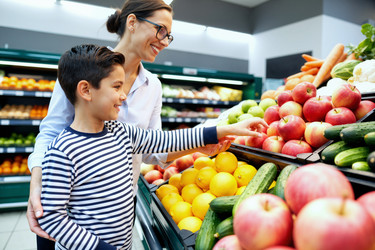 Женщина с сыном выбирает свежие продукты для здорового питания во время покупок в продуктовом магазине. - SeventyFour