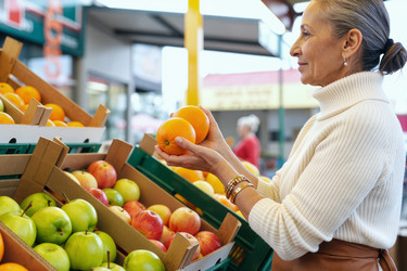Пожилая женщина выбирает свежие апельсины для здоровых покупок в продуктовом магазине. - SeventyFour