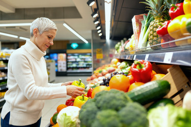 Женщина средних лет выбирает свежие продукты для здорового питания во время покупок в продуктовом магазине. - SeventyFour