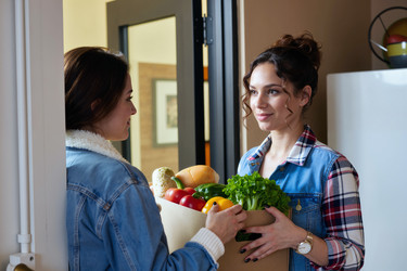 Взрослые женщины обмениваются доставленными продуктами у двери квартиры. - SeventyFour
