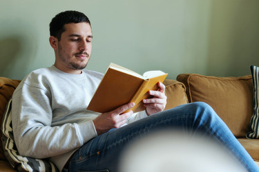 Взрослый мужчина читает книгу дома для отдыха и расслабления. - SeventyFour