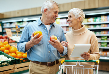 Пожилая пара сравнивает фрукты во время совместного похода в продуктовый магазин. - SeventyFour