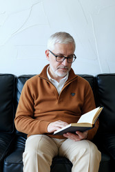 Пожилой мужчина читает книги дома для удовольствия и непрерывного обучения. - DragonImagesAsia