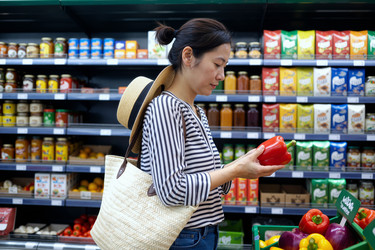 Взрослая азиатка рассматривает болгарский перец во время похода в продуктовый магазин. - SeventyFour