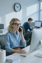 Взрослая женщина отвечает на телефонный звонок, работая в офисе. - AnnaStills