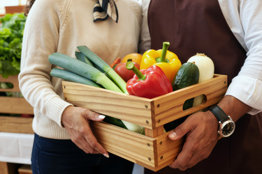 Взрослая пара держит ящик со свежими овощами для продажи в продуктовом магазине. - SeventyFour