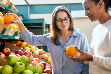 Взрослые женщины выбирают свежие фрукты для здоровых покупок в продуктовом магазине. - SeventyFour