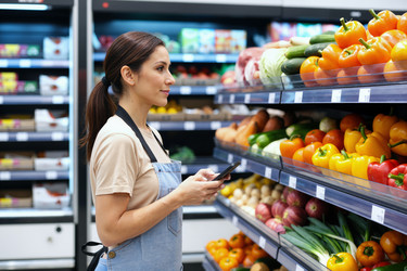 Женщина проверяет наличие продуктов в супермаркете с помощью смартфона. - SeventyFour