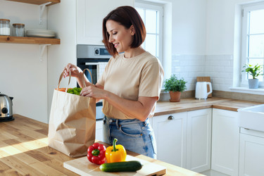 Взрослая женщина распаковывает доставленные продукты на домашней кухне. - SeventyFour